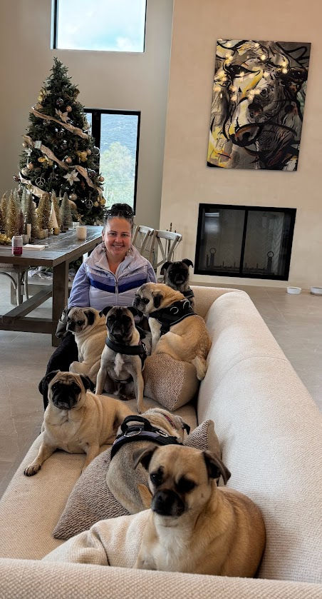 Sabrina, founder of Pawtrait Booth, sitting with her pugs on a couch in front of a decorated Christmas tree